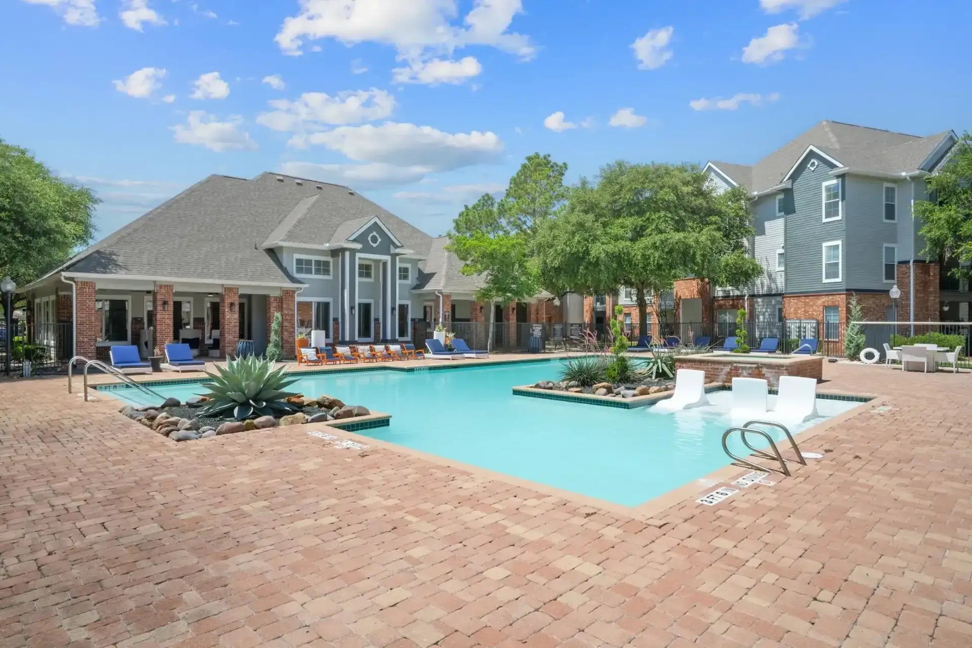 Swimming pool at an apartment complex, blue water, brick patio, blue building, blue sky, trees.