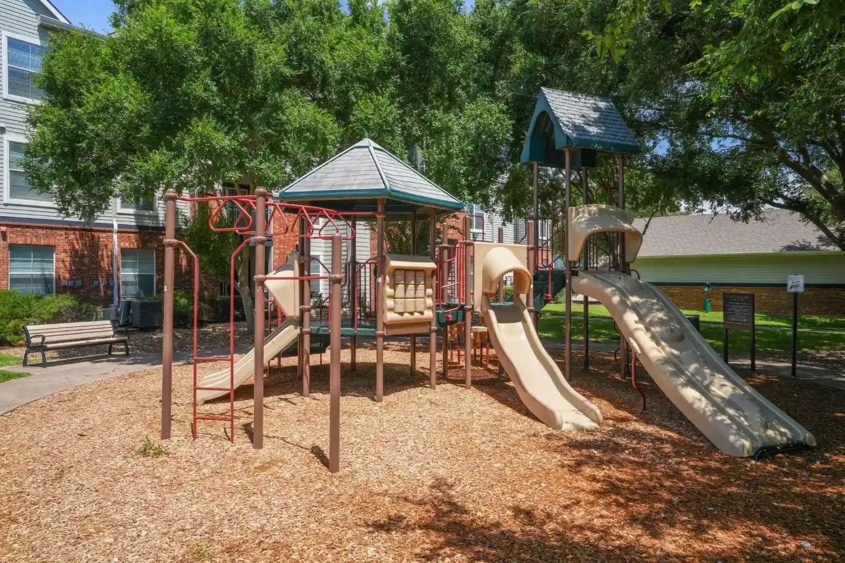 Playground with slides, climbing structures, and wood chips, in an outdoor setting.
