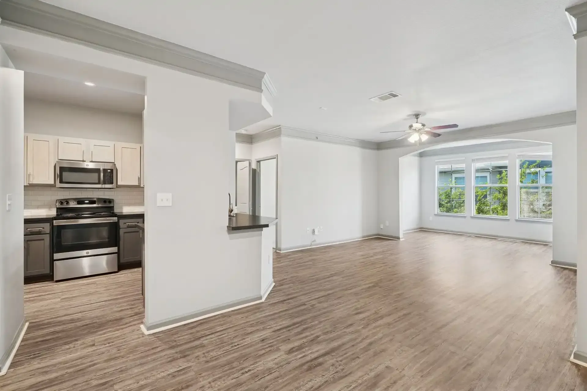 Open-concept living space with kitchen visible. Light gray walls, wood-look flooring, and stainless steel appliances.