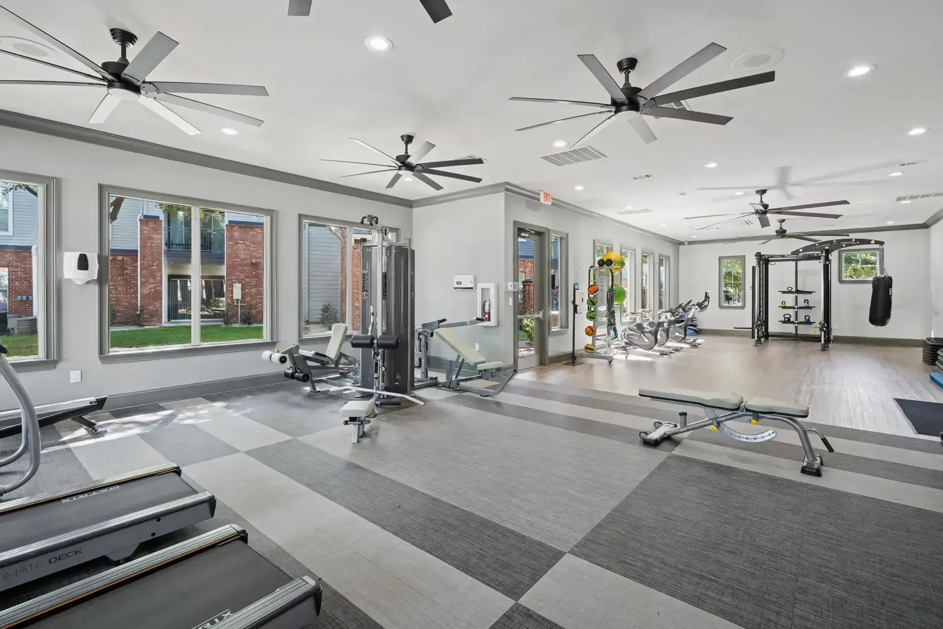 Gym interior with exercise equipment, gray and blue color scheme, windows, and ceiling fans.