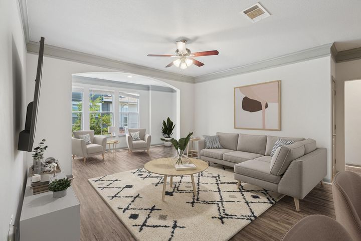 Living room with light gray sofa, rug, chairs, and coffee table, with a view to a sunroom.