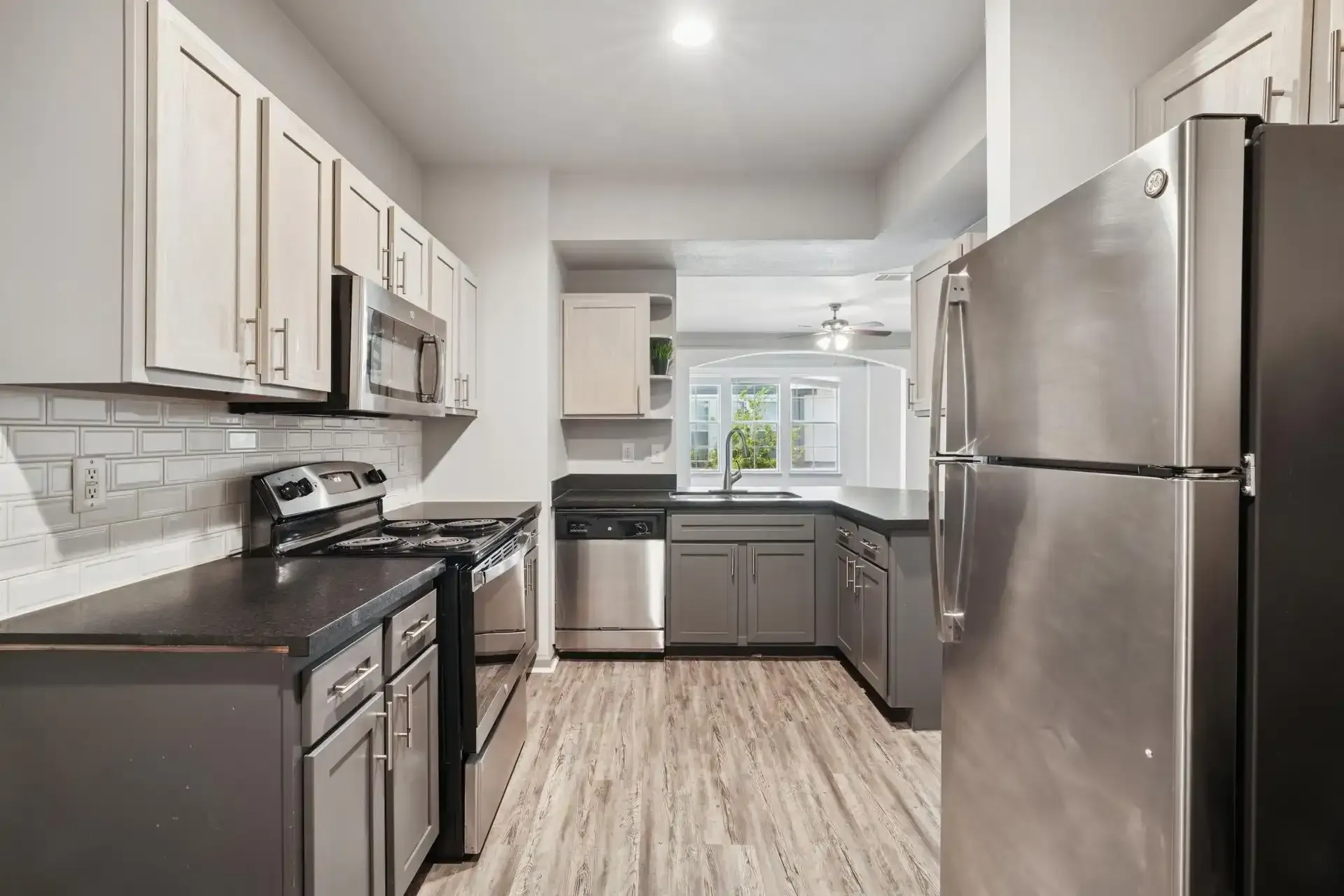 Modern kitchen with gray cabinets, stainless steel appliances, and light wood-look flooring.