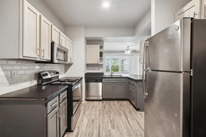 Modern kitchen with gray cabinets, stainless steel appliances, and light wood-look flooring.