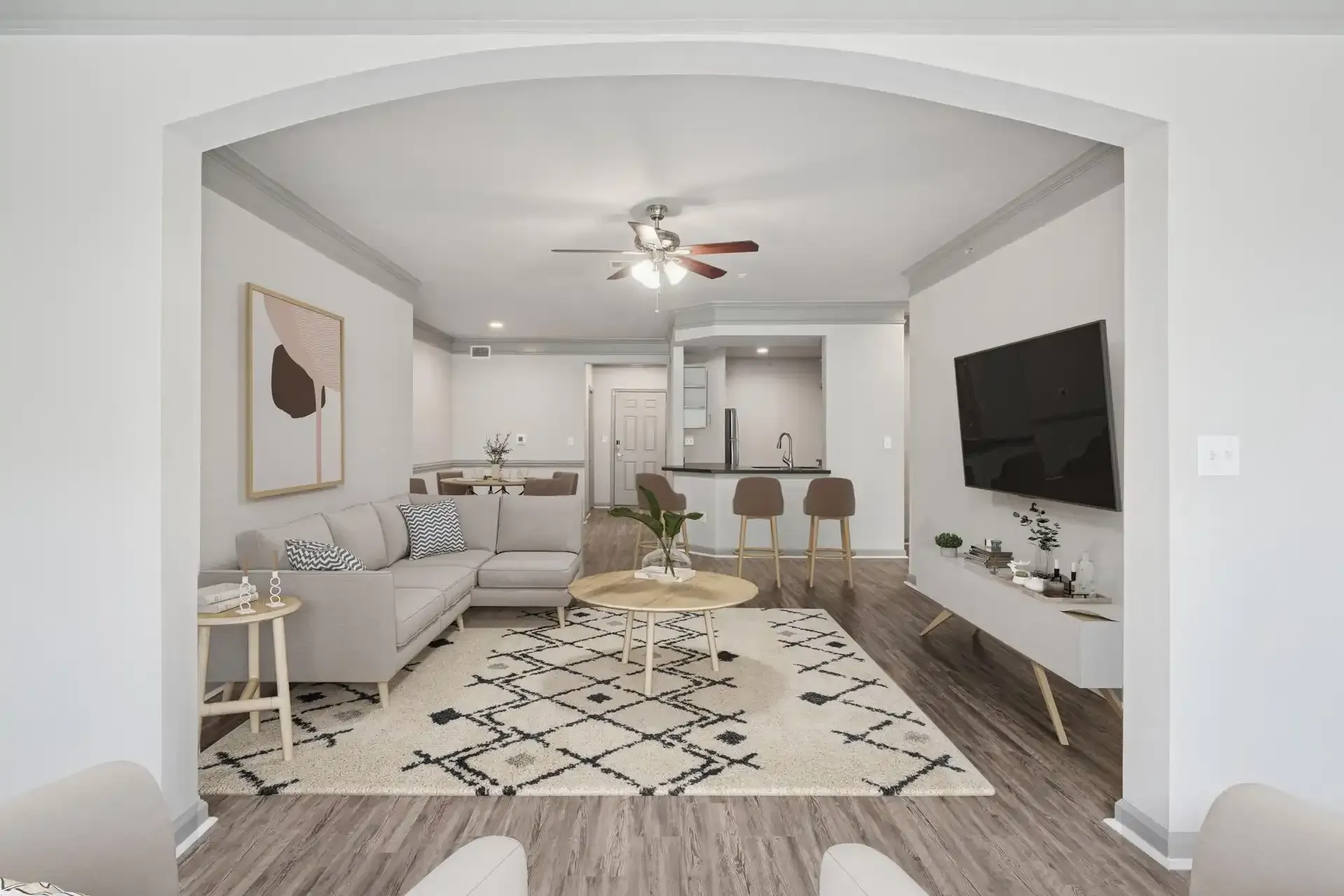 Living room with gray sectional, TV, rug, and open kitchen through an archway.