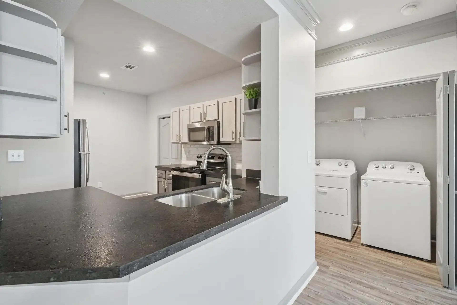 Kitchen and laundry area in apartment with gray cabinets, black countertop, and white washer and dryer.