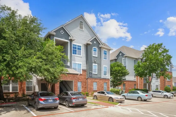 Apartment building with brick and blue siding; cars parked out front; blue sky.
