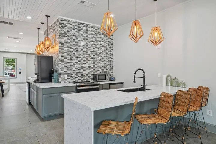 Communal kitchen with island seating, pendant lights, and a tiled backsplash.