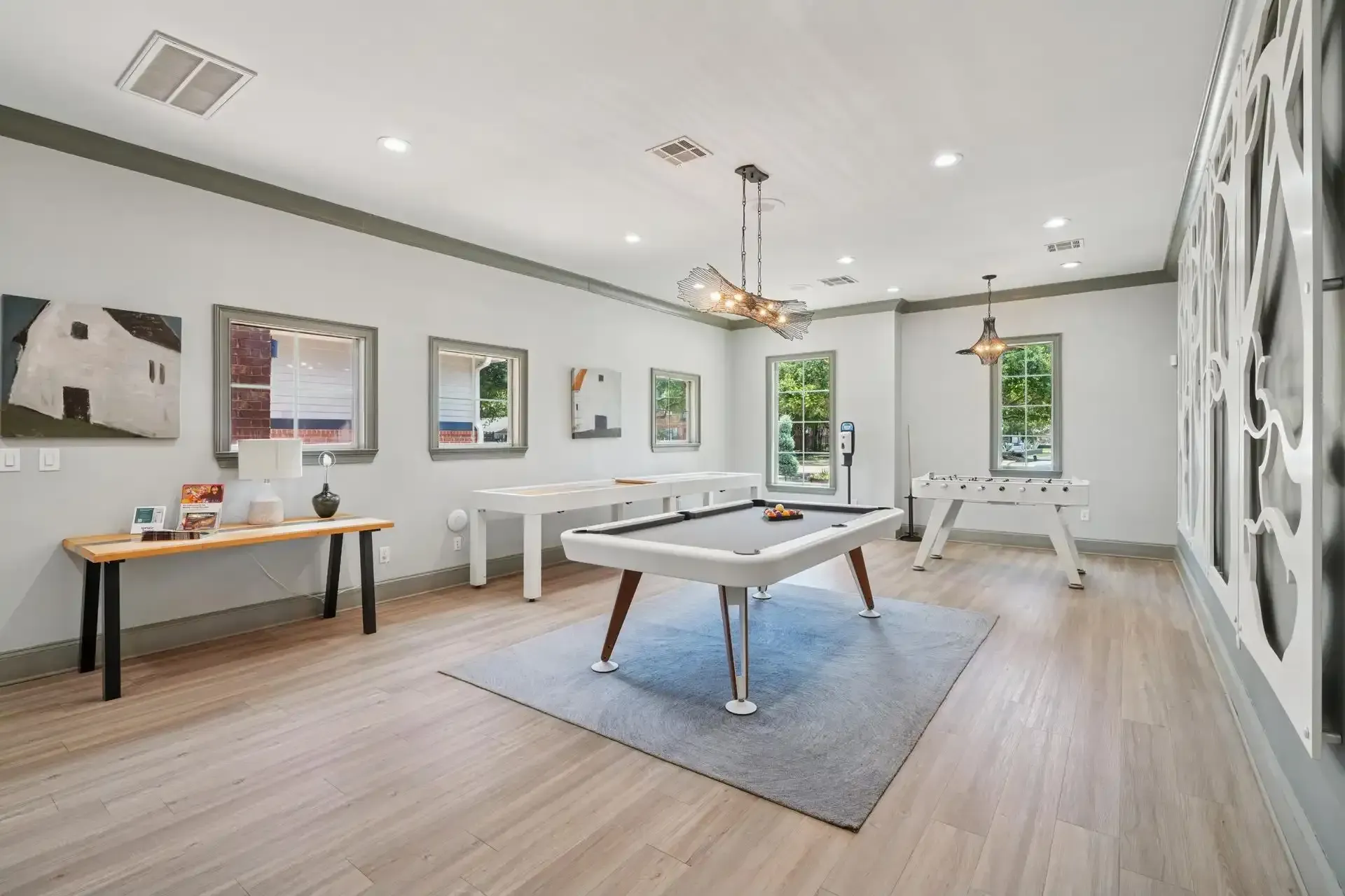 Game room with pool table, foosball, and tables, with artwork on the walls and wood floors.