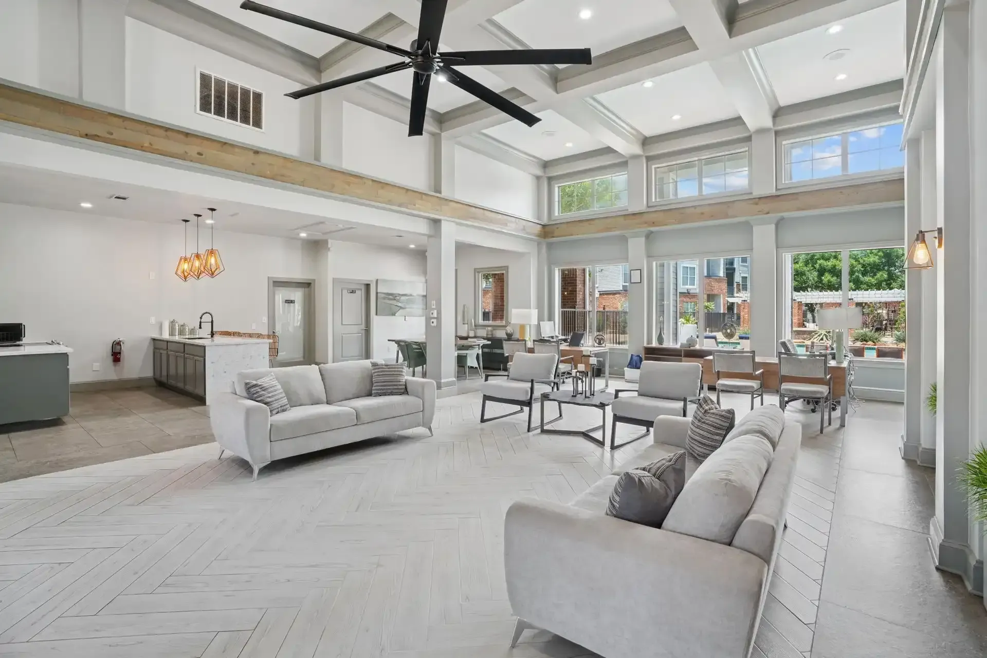 Spacious apartment lounge with seating areas, large fan, and windows.