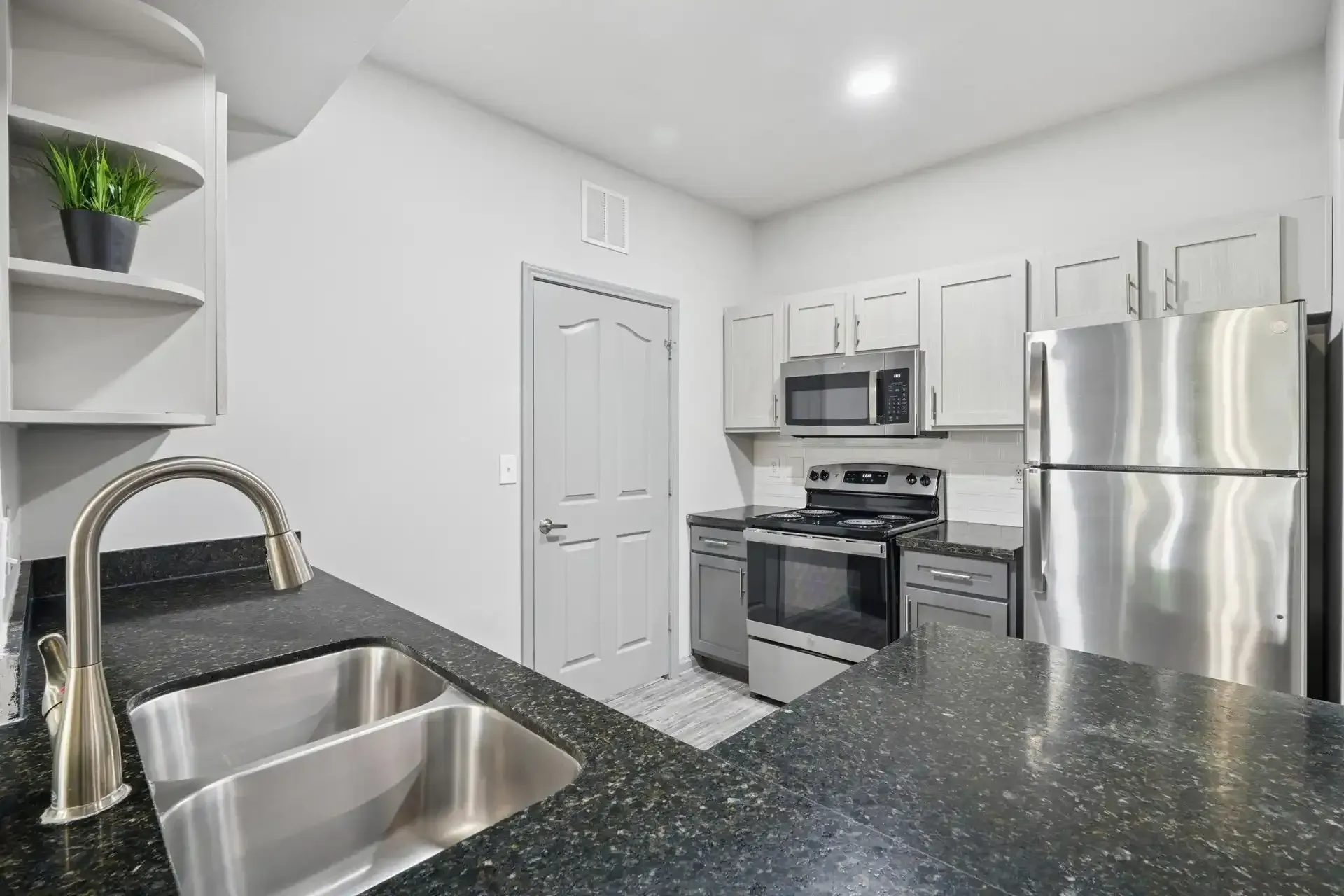 Modern kitchen with stainless steel appliances, gray cabinets, and black speckled countertops.