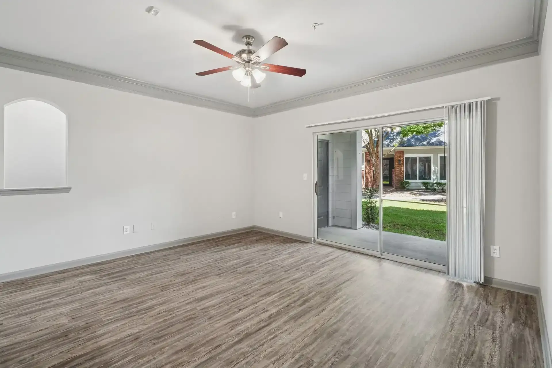 Empty room with wood-look flooring, sliding glass door, and ceiling fan, looking out to a grassy yard.