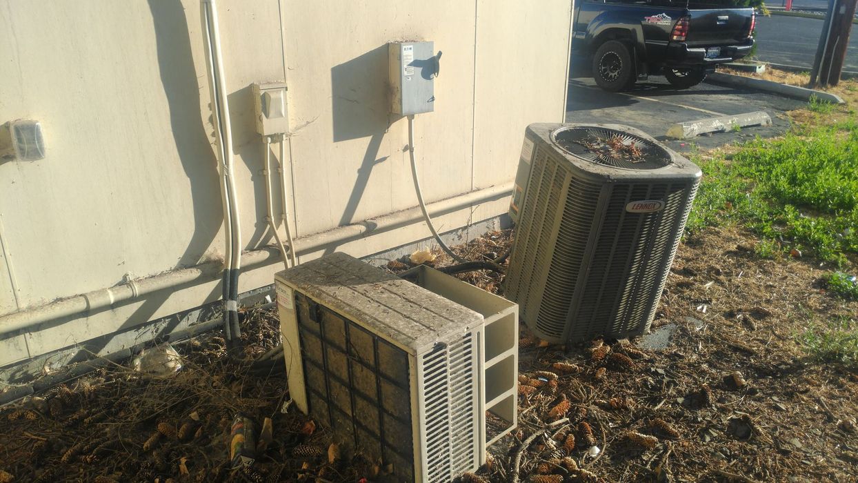 Two air conditioners are sitting on the ground in front of a building.