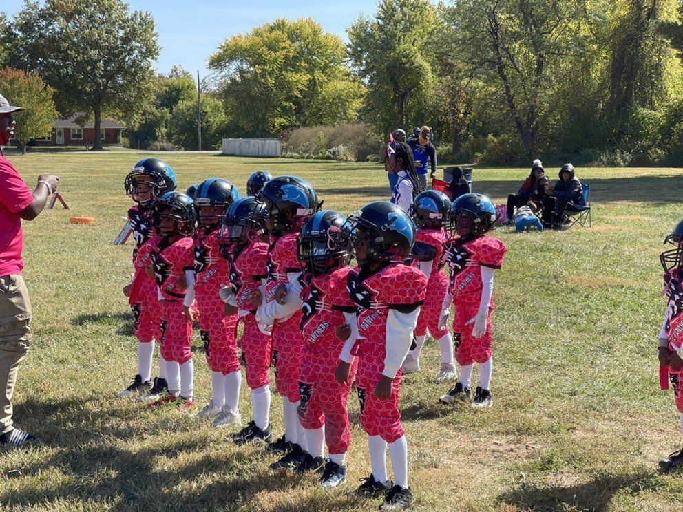 Young football players in pink and black uniforms on a grassy field.