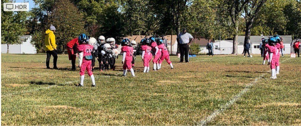 Youth football game on a grass field. Players in pink uniforms are in formation.