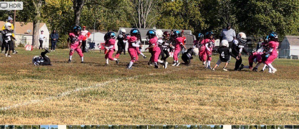 Youth football game with teams in pink and black uniforms on a grassy field.