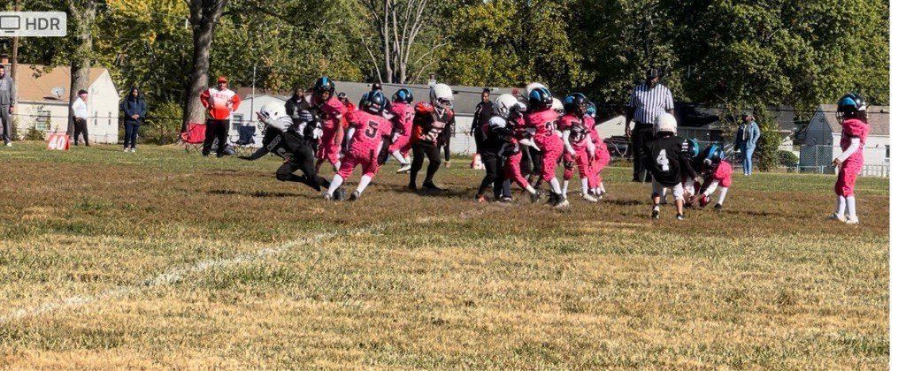 Youth football players in pink and black uniforms on a dirt field.