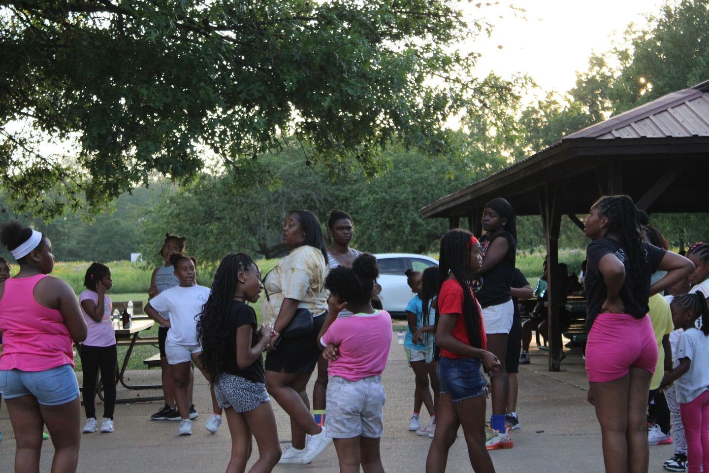 Group of young girls and women in a park, some dancing under a shelter.