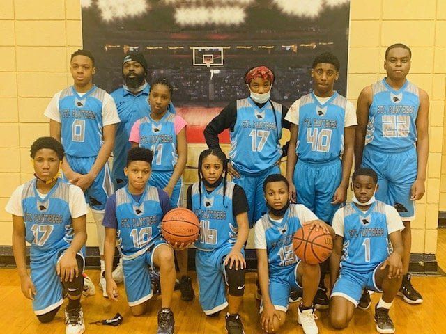Basketball team posing in blue uniforms. Team members and coaches in a gym.