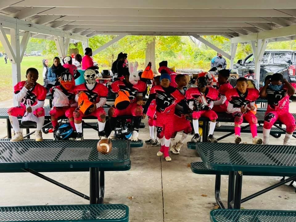 Youth football team in pink and white uniforms at a picnic shelter, some with masks, holding a football.