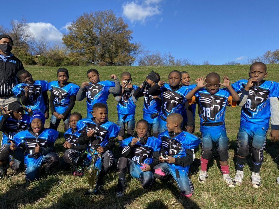 Youth football team in blue uniforms poses on a grassy hill with trophy; sunny day.