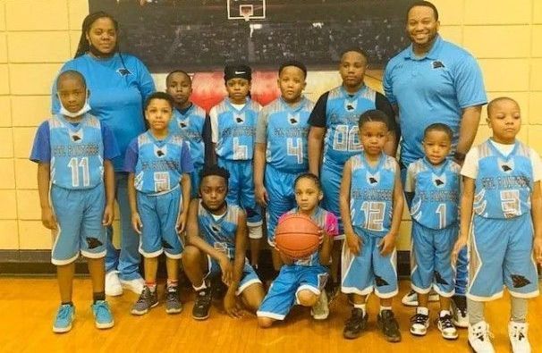 Youth basketball team in blue uniforms posing with coaches in a gym.