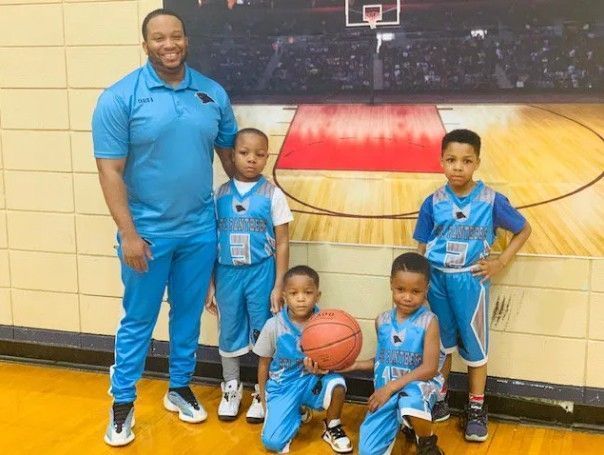 Basketball coach with four young players, all in blue uniforms, posing on court.