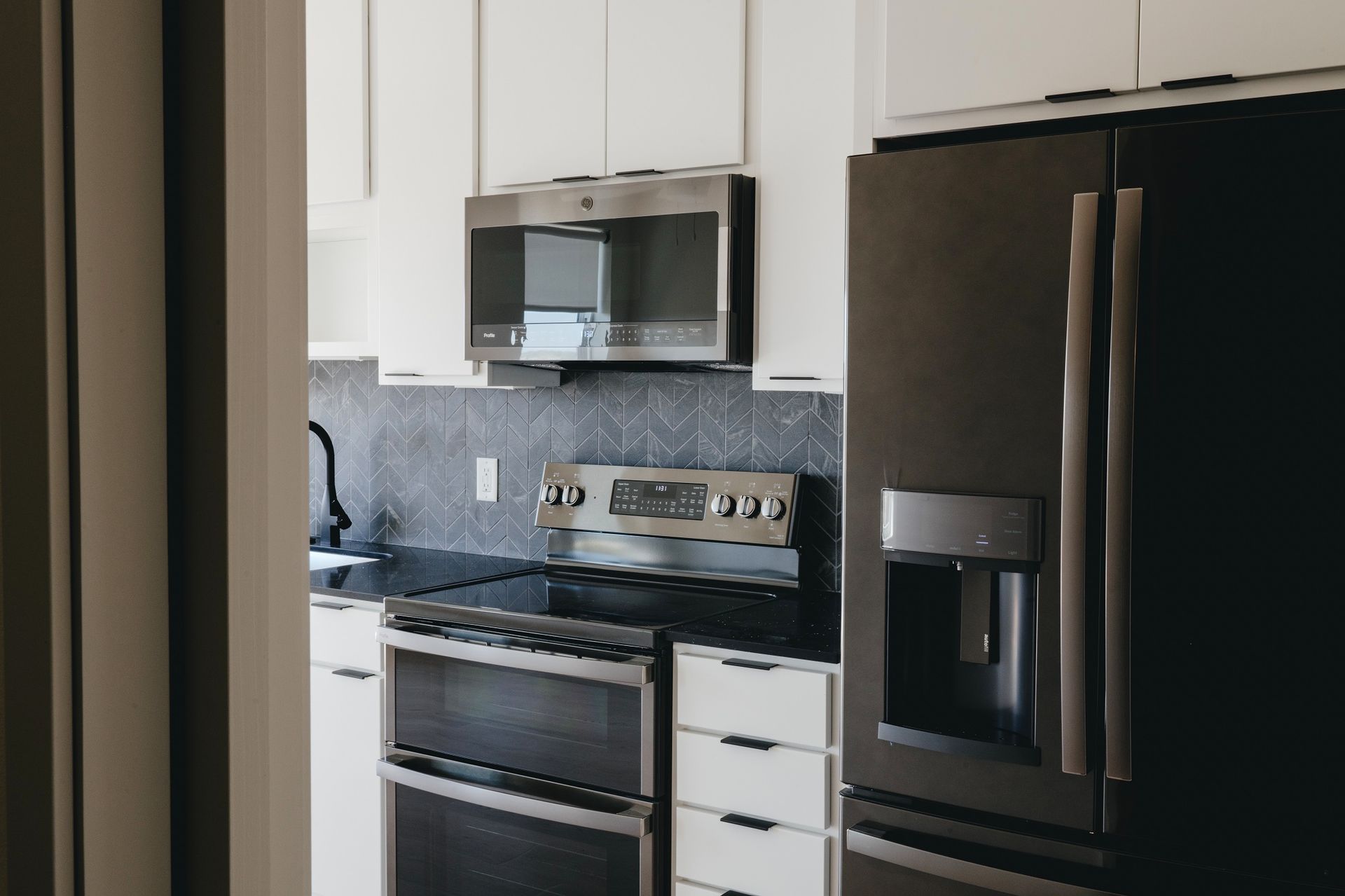 Modern kitchen with white cabinets, black appliances, and dark backsplash at Revelry in Madison WI.