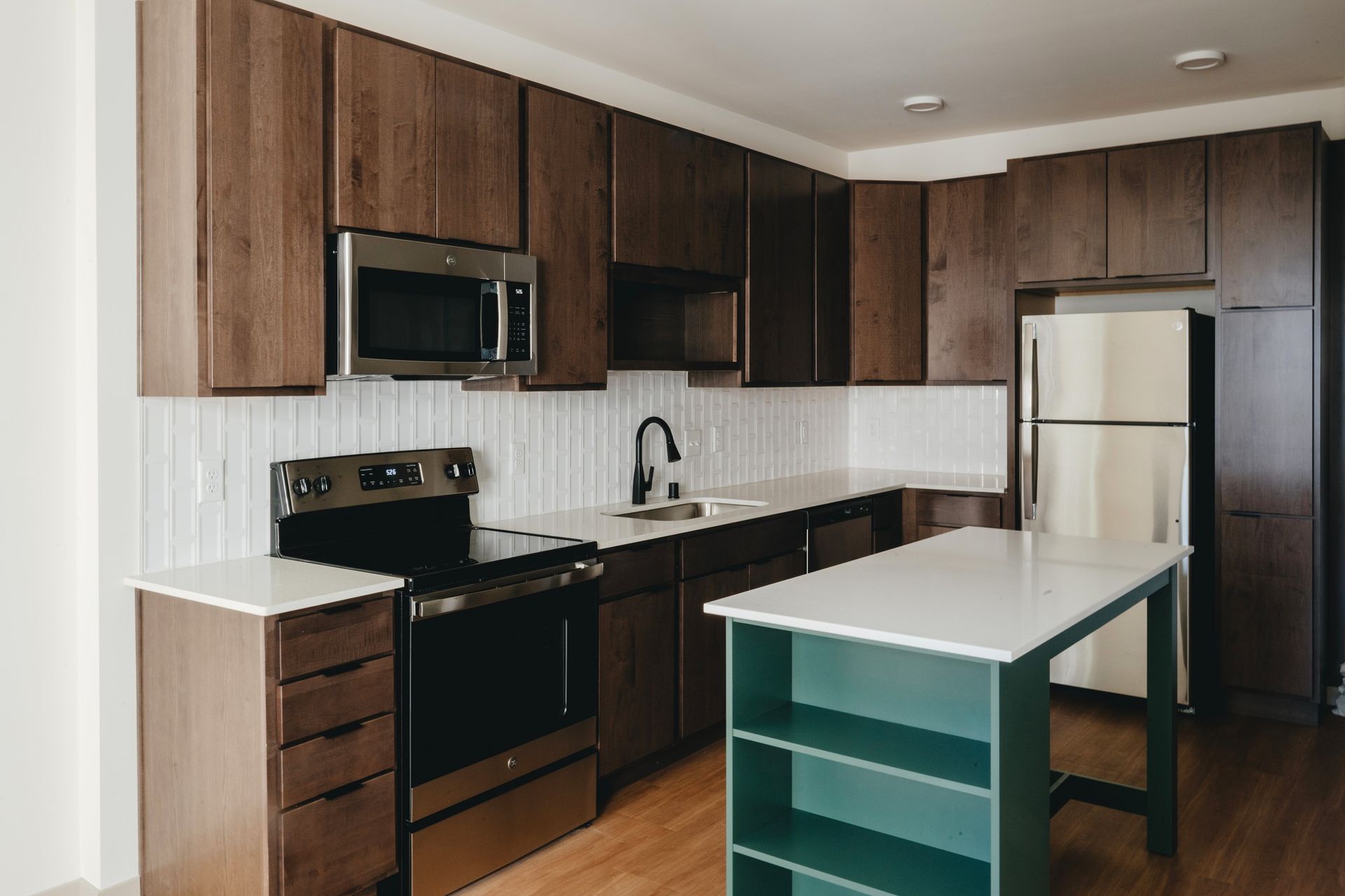 Modern kitchen with dark brown cabinets, stainless steel appliances, white countertops, and a teal island at Revelry in Madison WI.