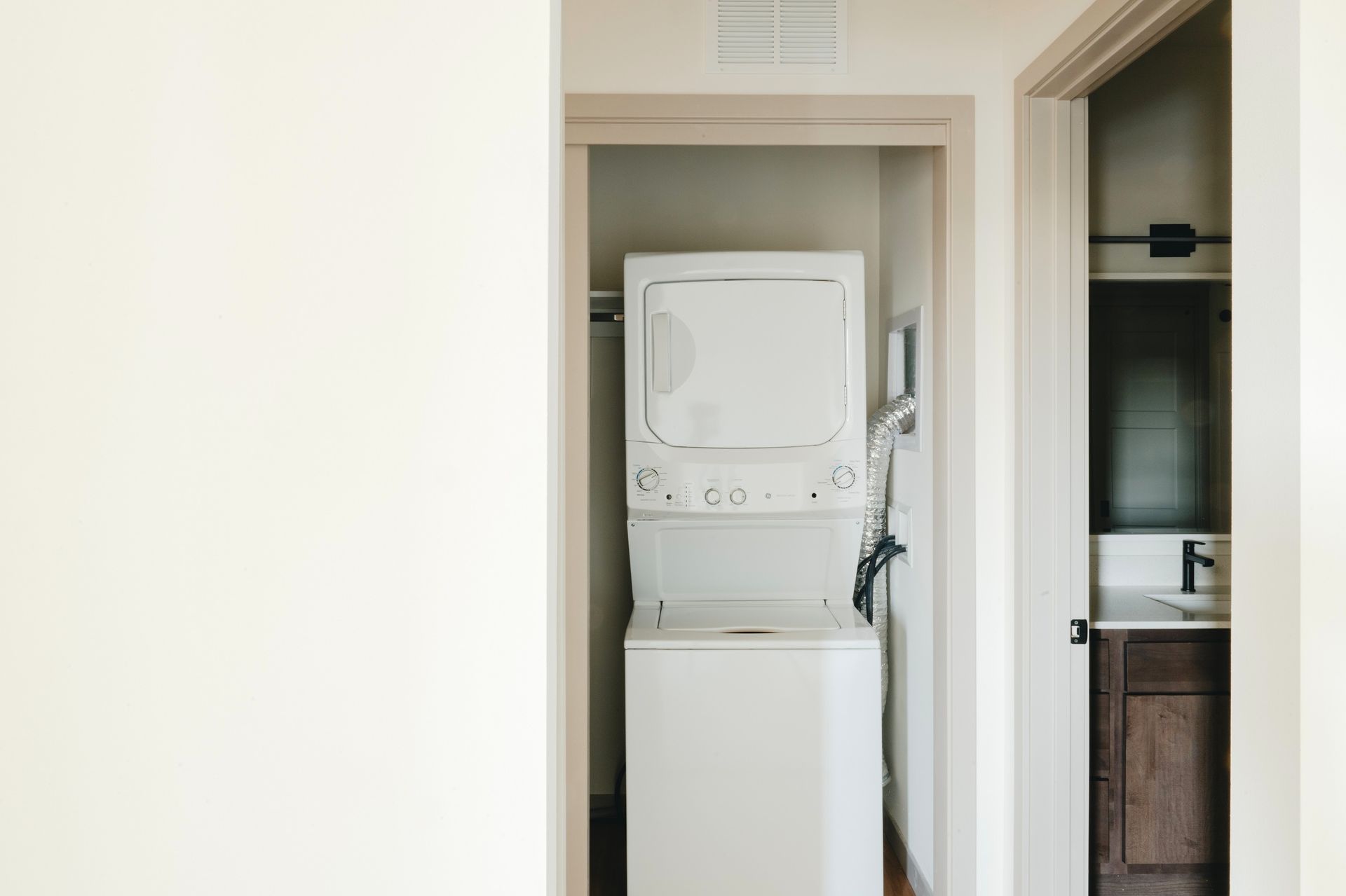 White stacked washer and dryer in a small closet, next to a bathroom door with a dark vanity at Revelry in Madison WI.
