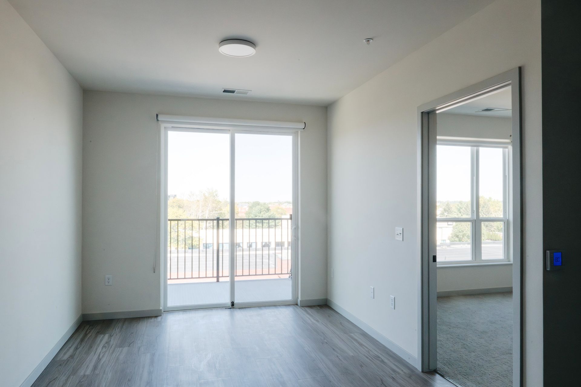 Empty room with sliding glass door to balcony, open doorway, light wood floor, white walls at Revelry in Madison WI.
