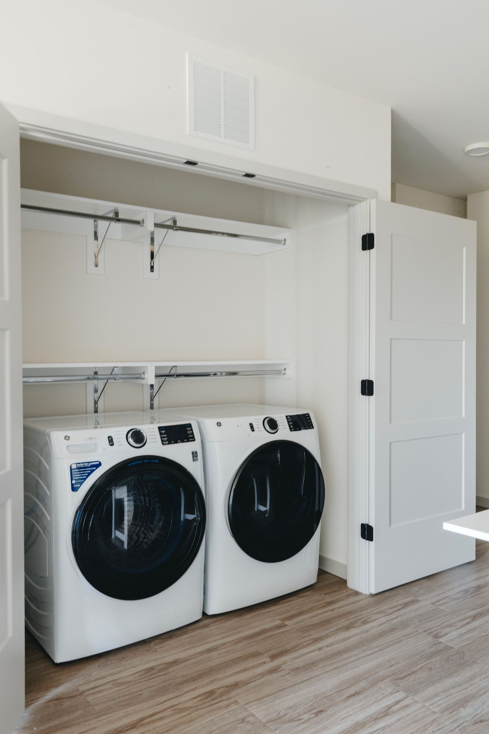 Laundry closet with front-loading white washer and dryer. White shelves and rod above. Doors on the right at Revelry in Madison WI.