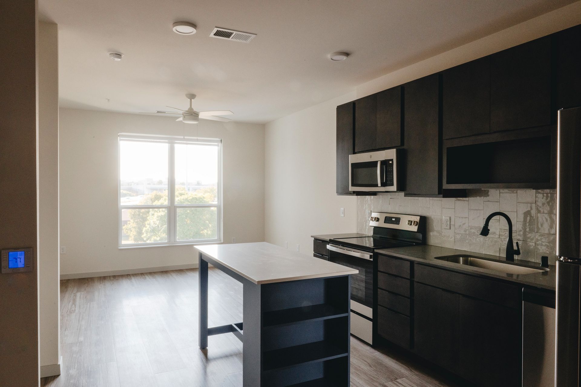 Modern kitchen with dark cabinets, white island, and a window view at Revelry in Madison WI.