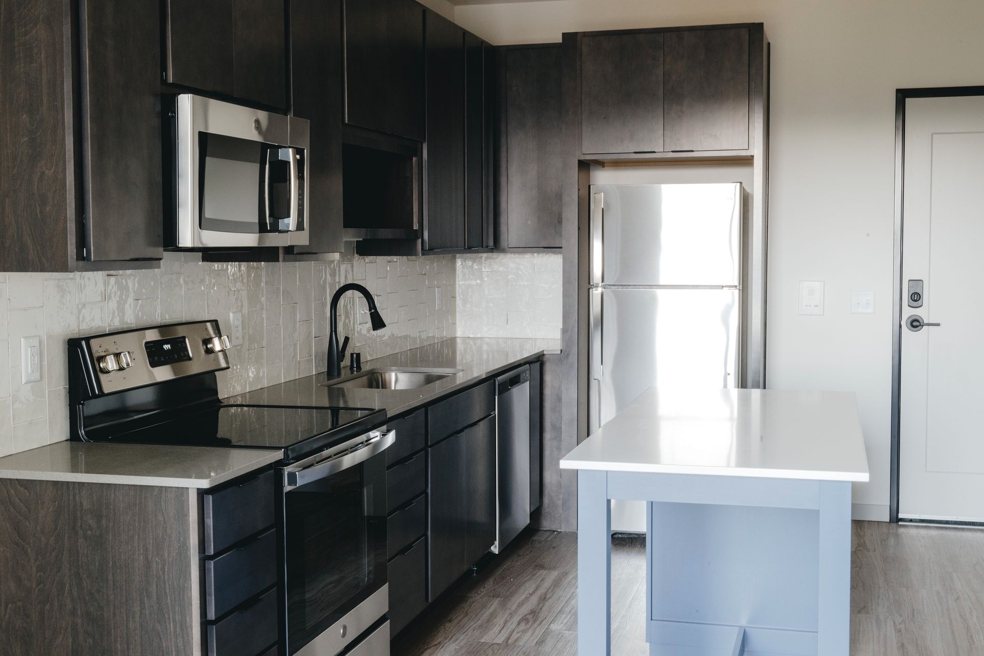 Modern kitchen with dark cabinets, stainless steel appliances, and white countertop island at Revelry in Madison WI.