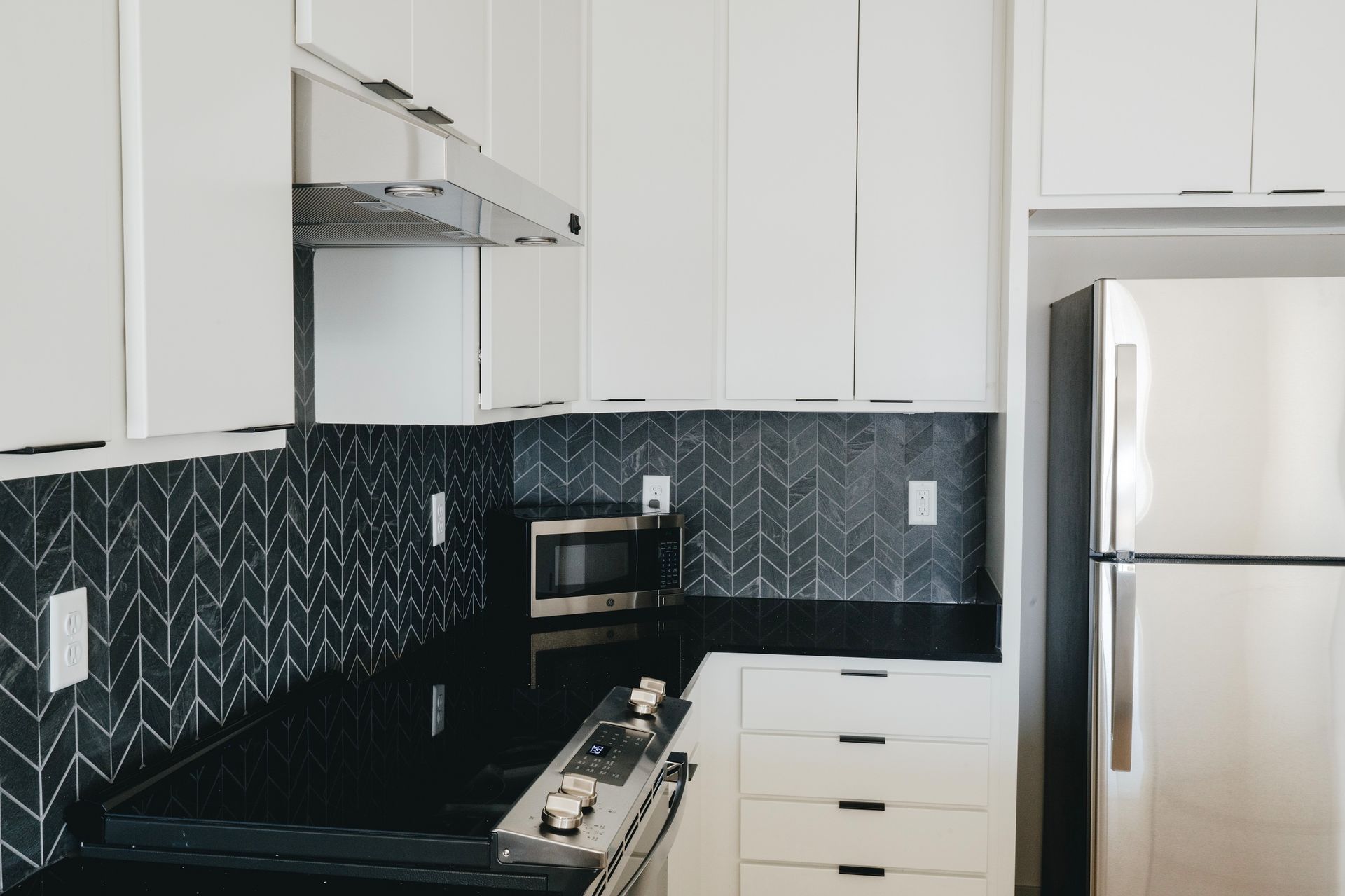 Modern white kitchen with black countertops, backsplash, and stainless steel appliances at Revelry in Madison WI.