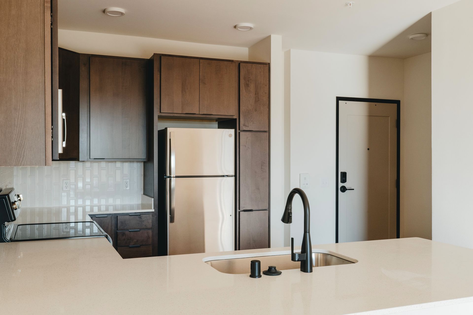 Modern kitchen with dark wood cabinets, stainless steel fridge, and black faucet at Revelry in Madison WI.