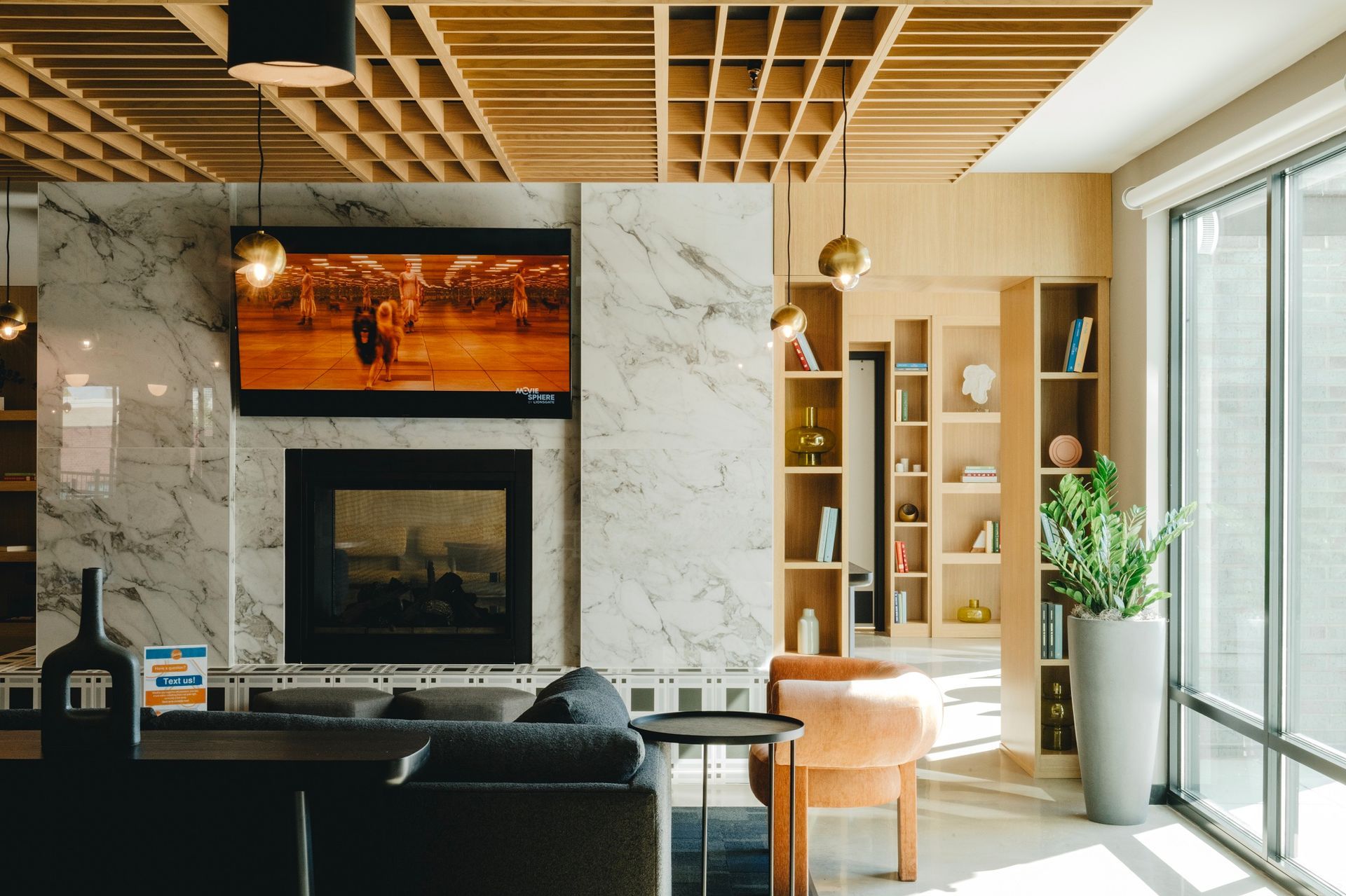 Living room with fireplace, TV, built-in shelves, and a large window. Modern design with wood, marble, and gold accents at Revelry in Madison WI.