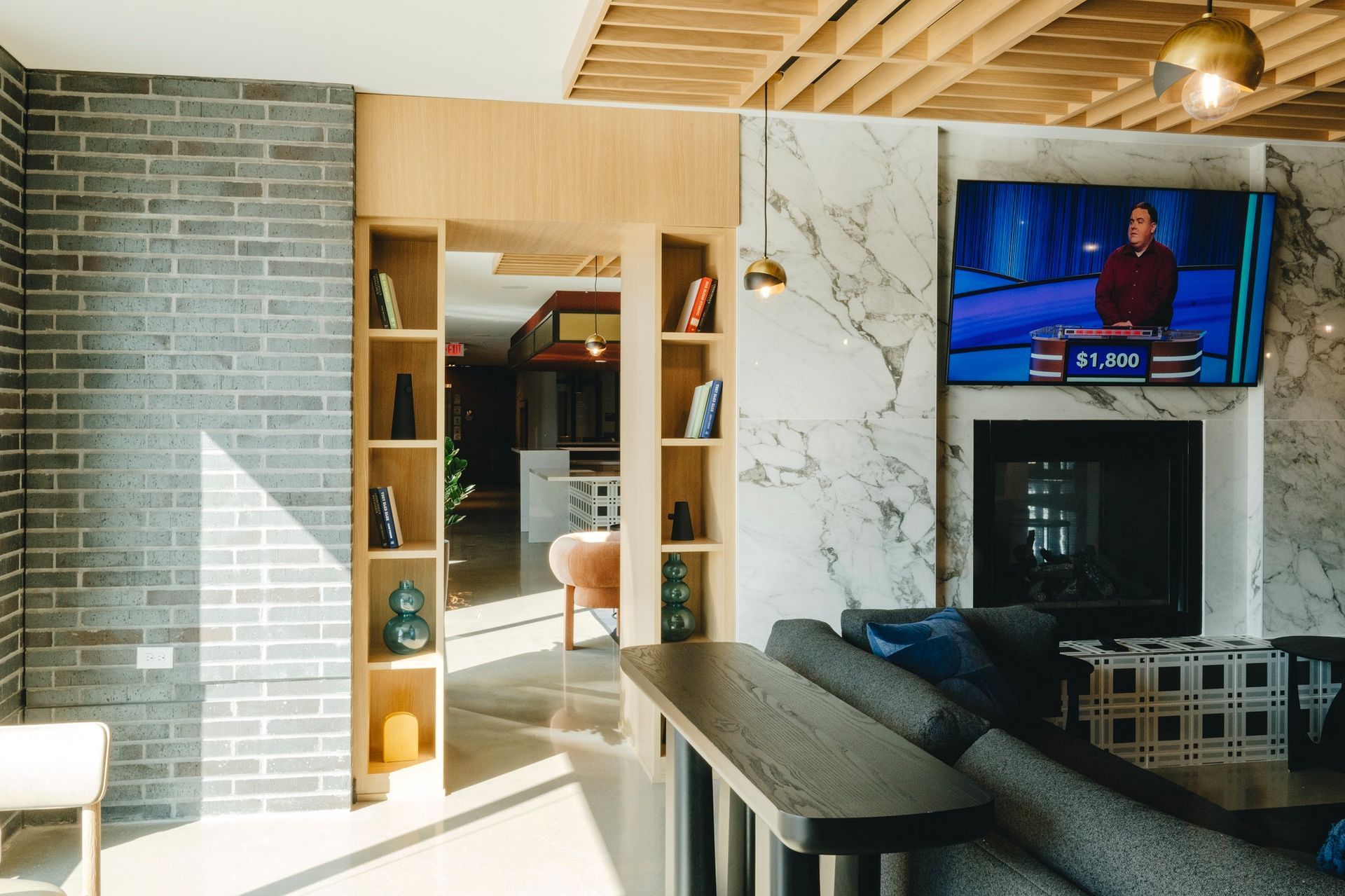 A modern living room with a brick wall, marble accent wall, and a TV playing Jeopardy.