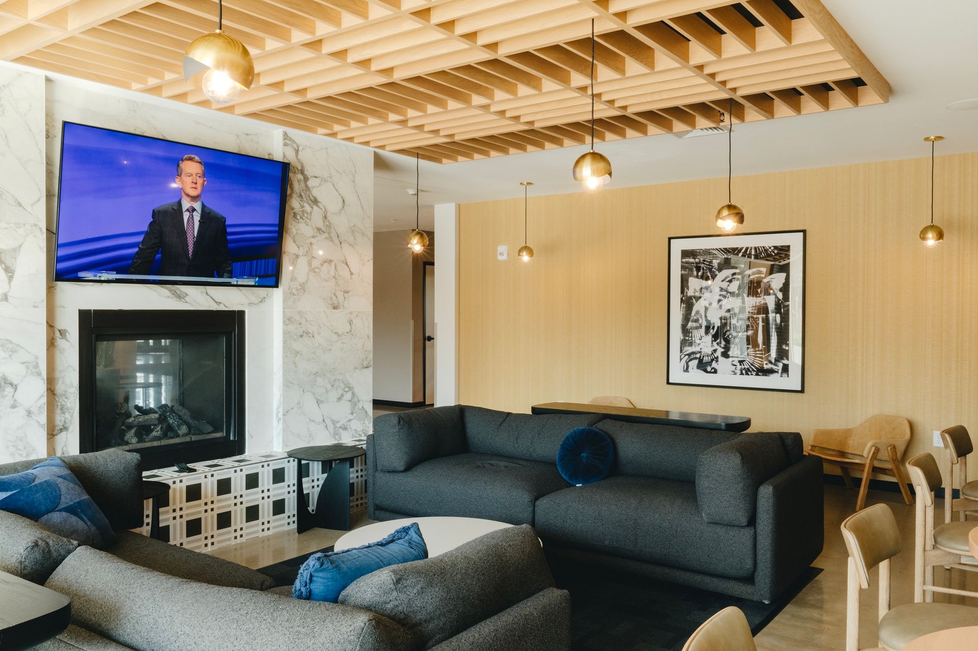 Living room with TV over fireplace, gray couches, art, gold accents, and wooden ceiling at Revelry in Madison WI.