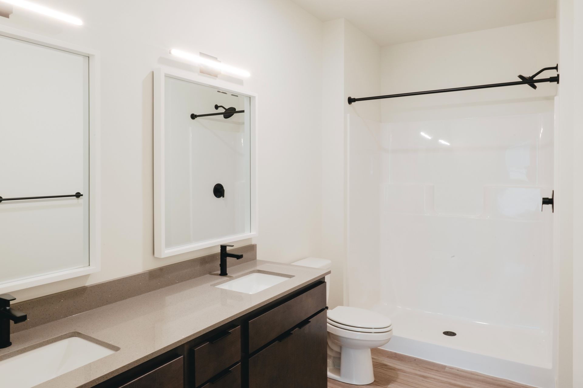 Modern bathroom with double sinks, a toilet, and a shower with black fixtures, neutral tones at Revelry in Madison WI.