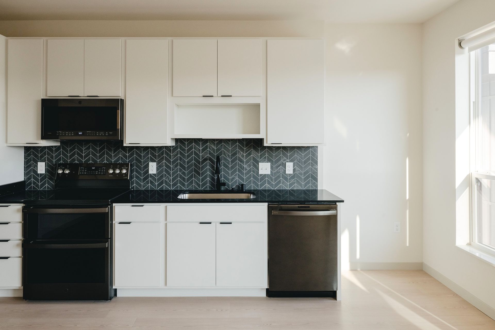 Modern kitchen with white cabinets, black appliances, and dark backsplash at Revelry in Madison WI.