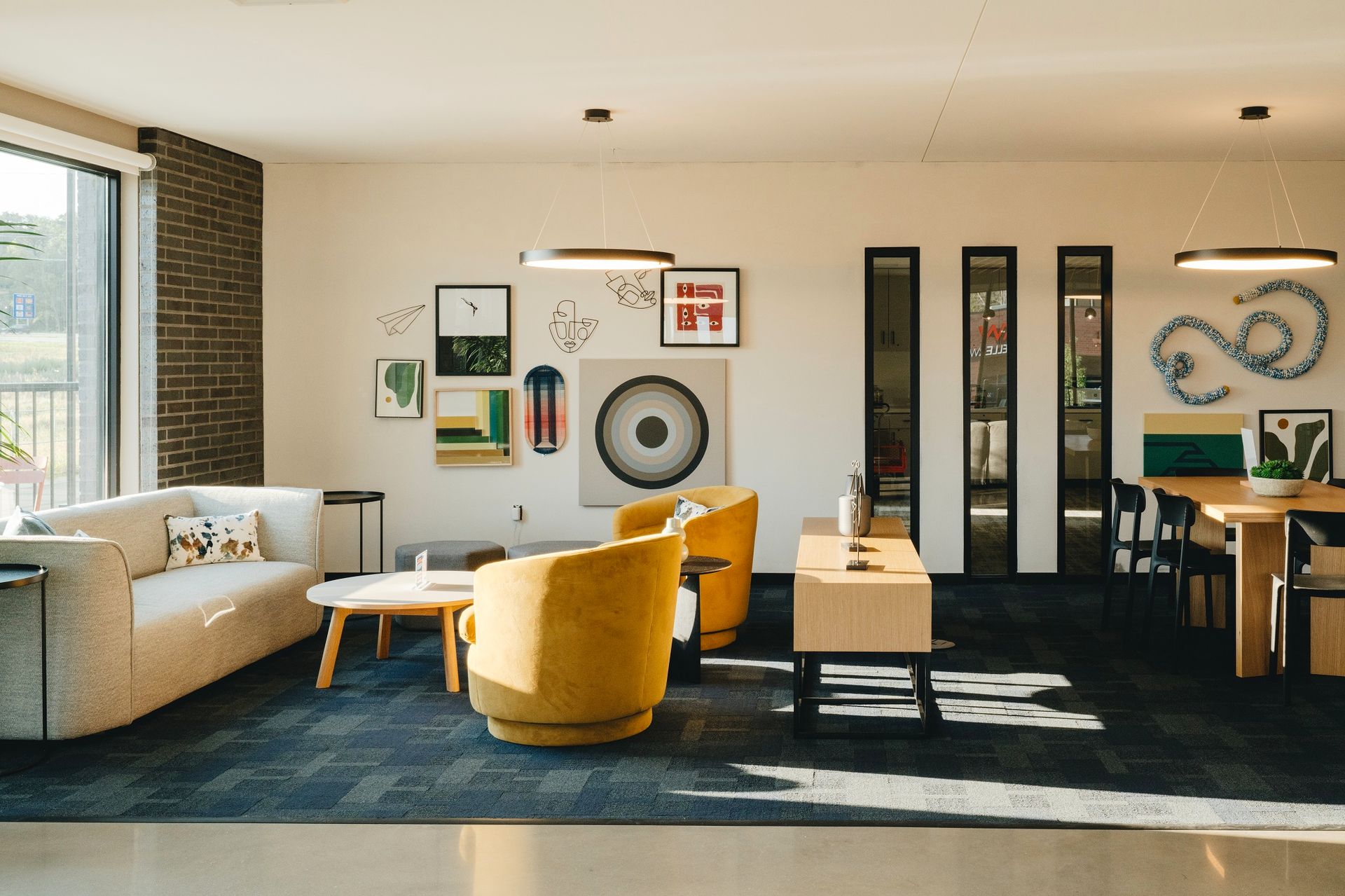 Modern living room with mustard-colored chairs, artwork, and dark blue rug. Sunny with a view at Revelry in Madison WI.