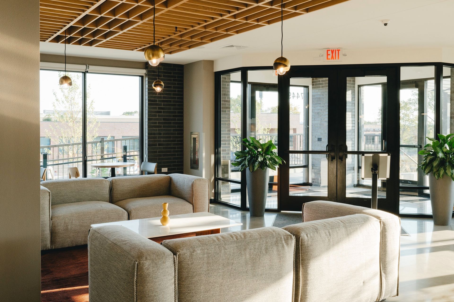 Cozy lounge area with light-colored couches, large windows, and decorative ceiling, leading to an exit at Revelry in Madison WI.