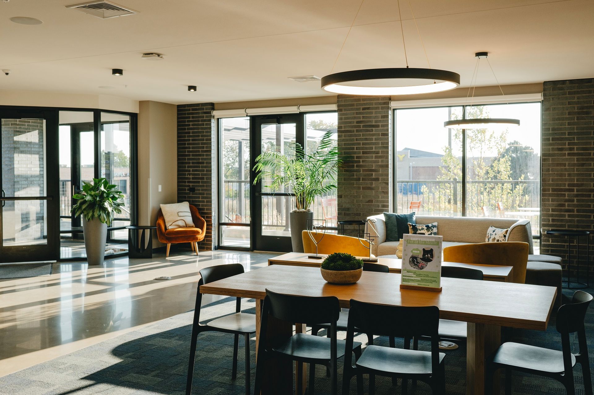 Spacious modern lobby with a long table, seating area, and large windows. Brick walls, natural light, and plants at Revelry in Madison WI.