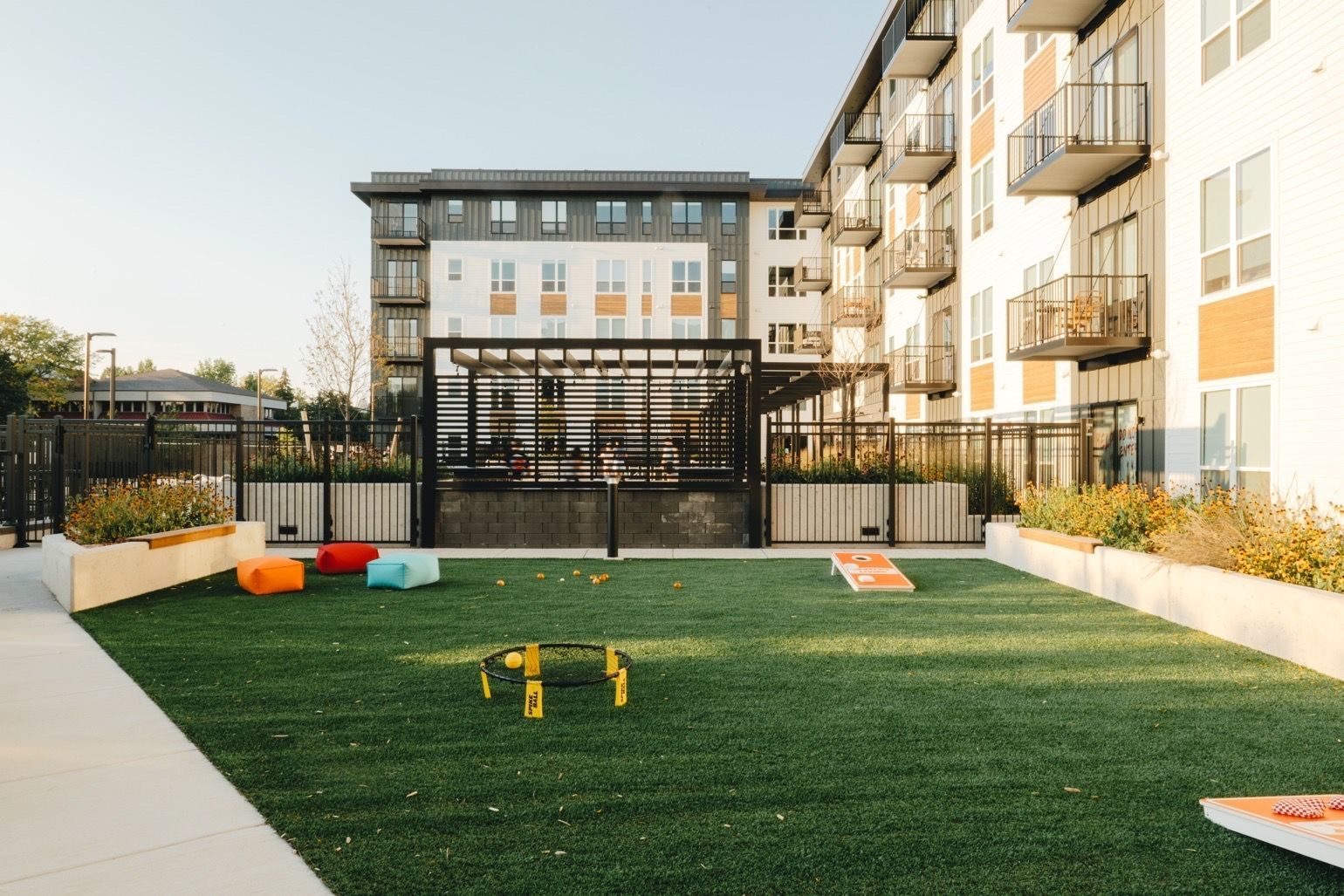 Apartment courtyard with turf, games, and colorful seating. Buildings in the background.