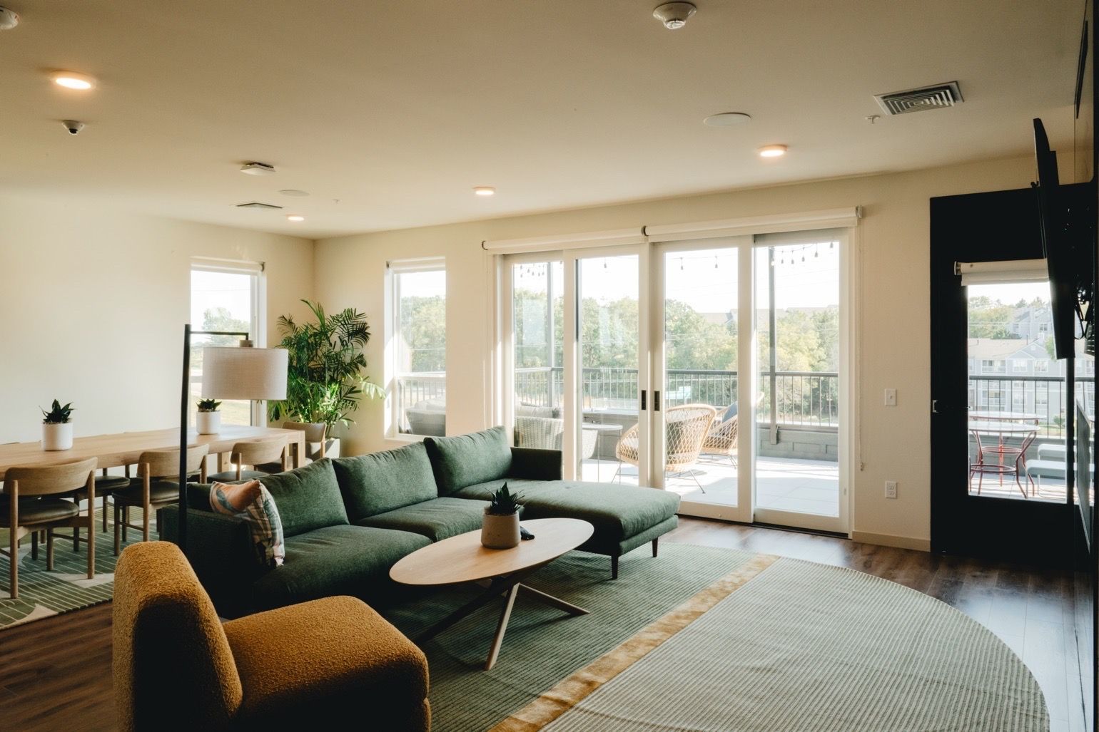 Spacious living room with green sectional sofa, open to a balcony. Neutral walls and wooden floors, lots of natural light at Revelry in Madison WI.