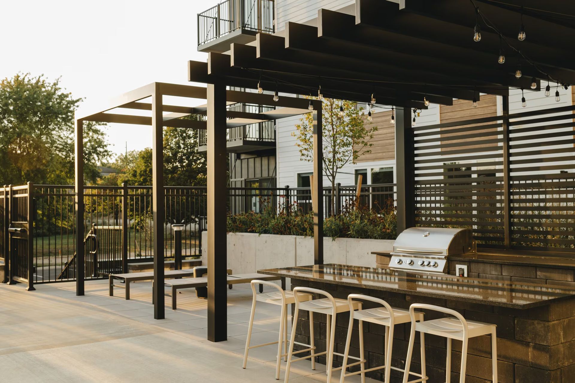 Outdoor grilling area with pergola, bar seating, and a view of an apartment building.