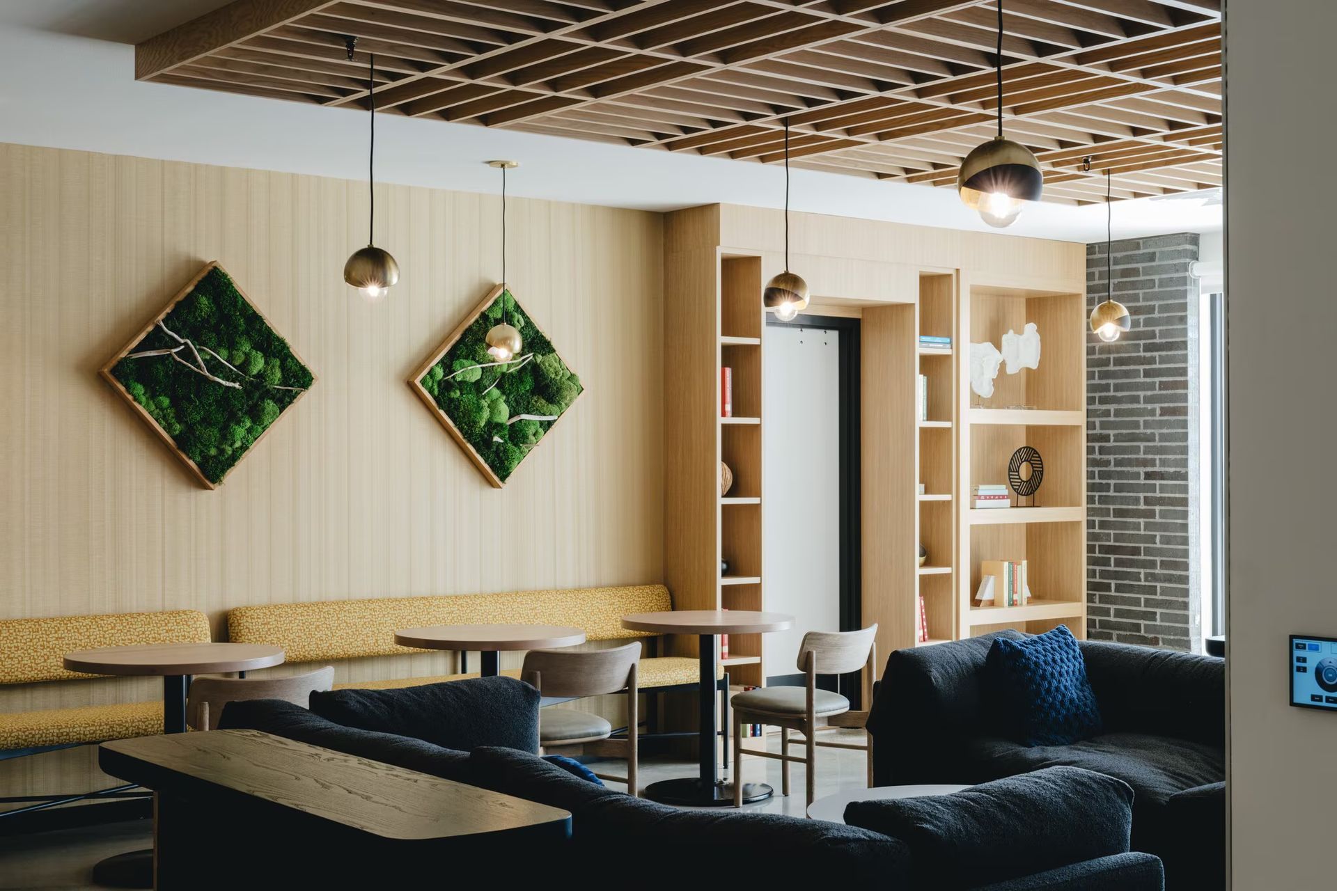 Modern lounge with built-in seating, moss art, hanging lights, and bookshelves.