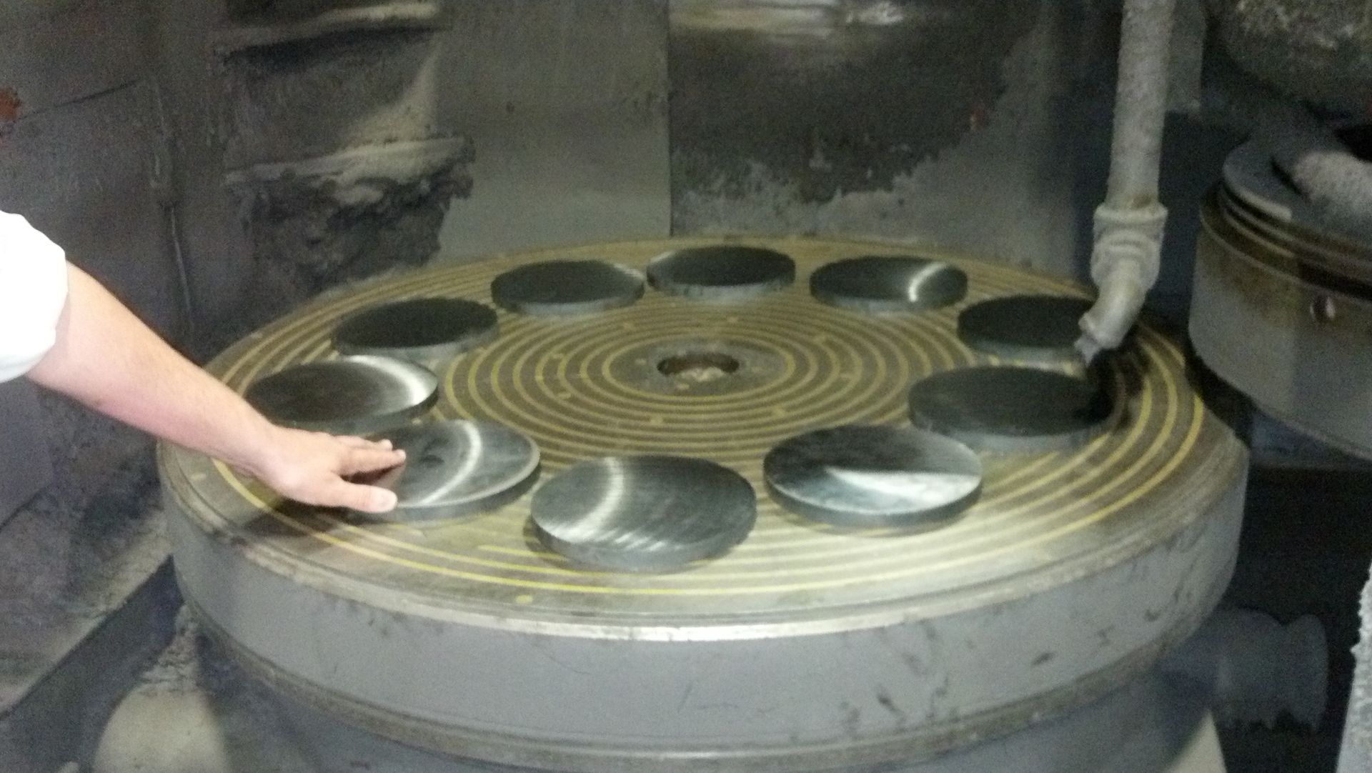 A person's hand touches a metal disc on a rotating grinding machine.