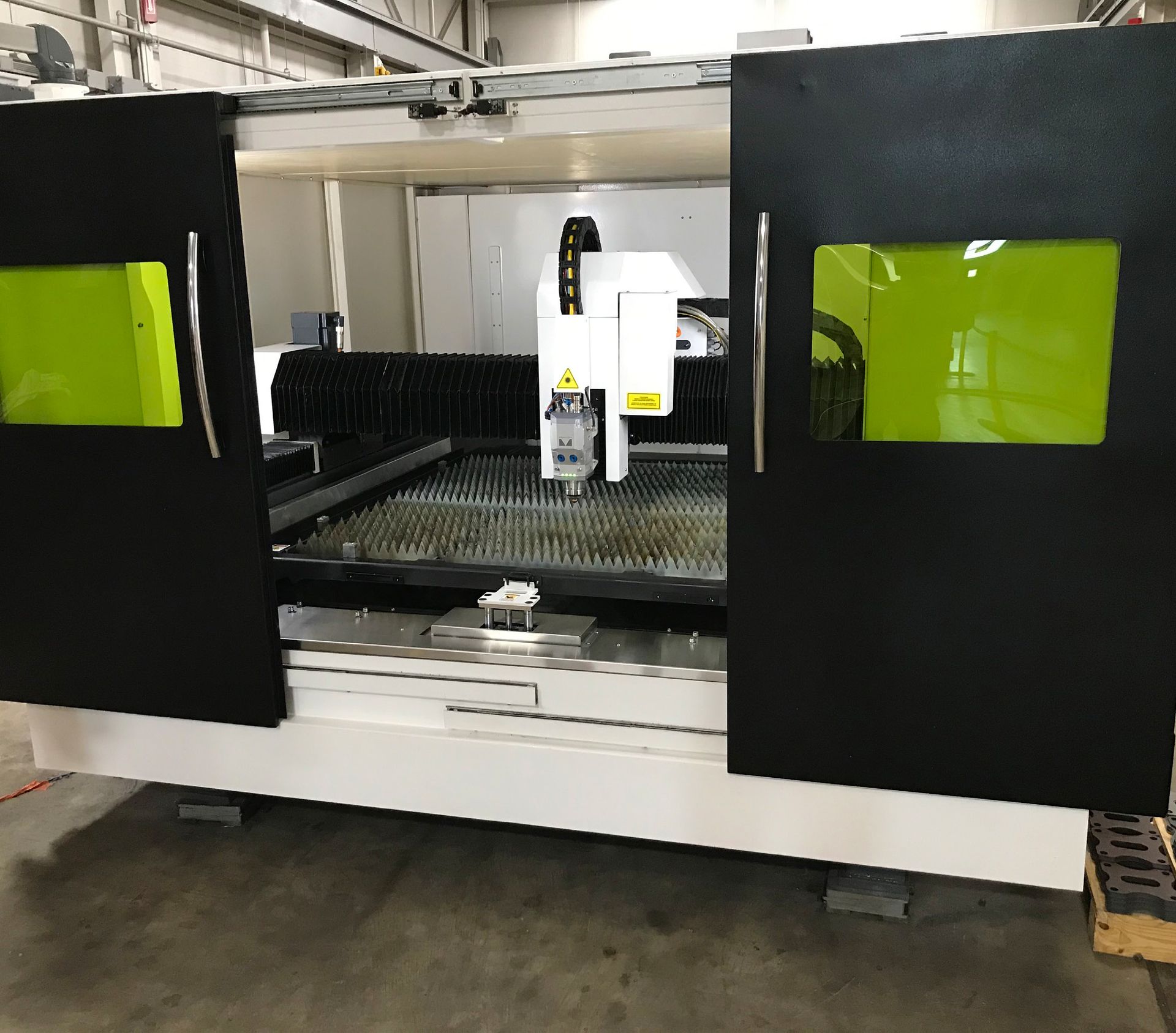 Large industrial laser cutter with black doors, white frame, and green viewing windows.