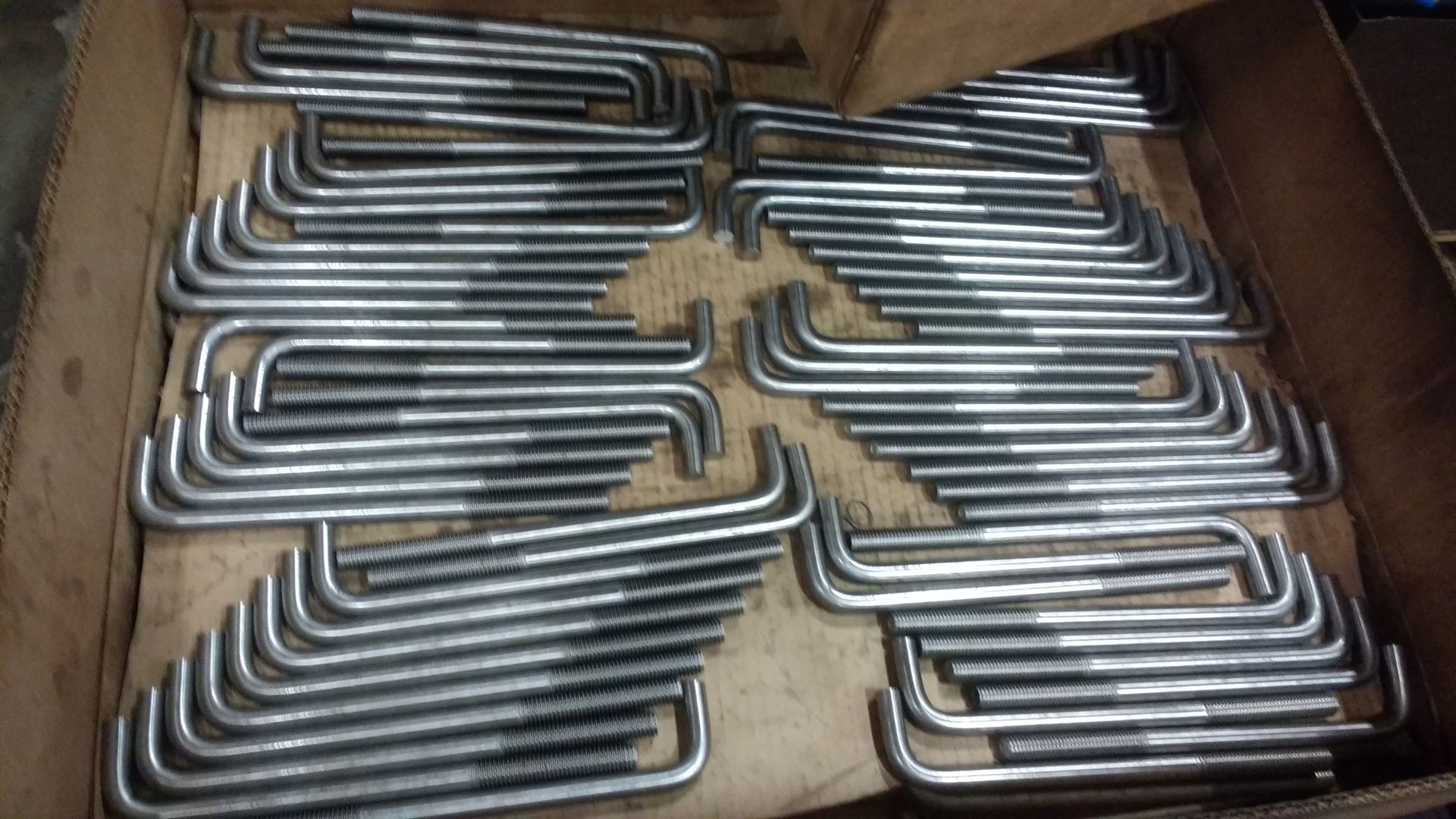 Box of shiny, bent metal bolts arranged in rows.